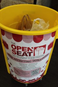 Large yellow bin with Open Seat sign on the outside. Bags of food on the inside. 